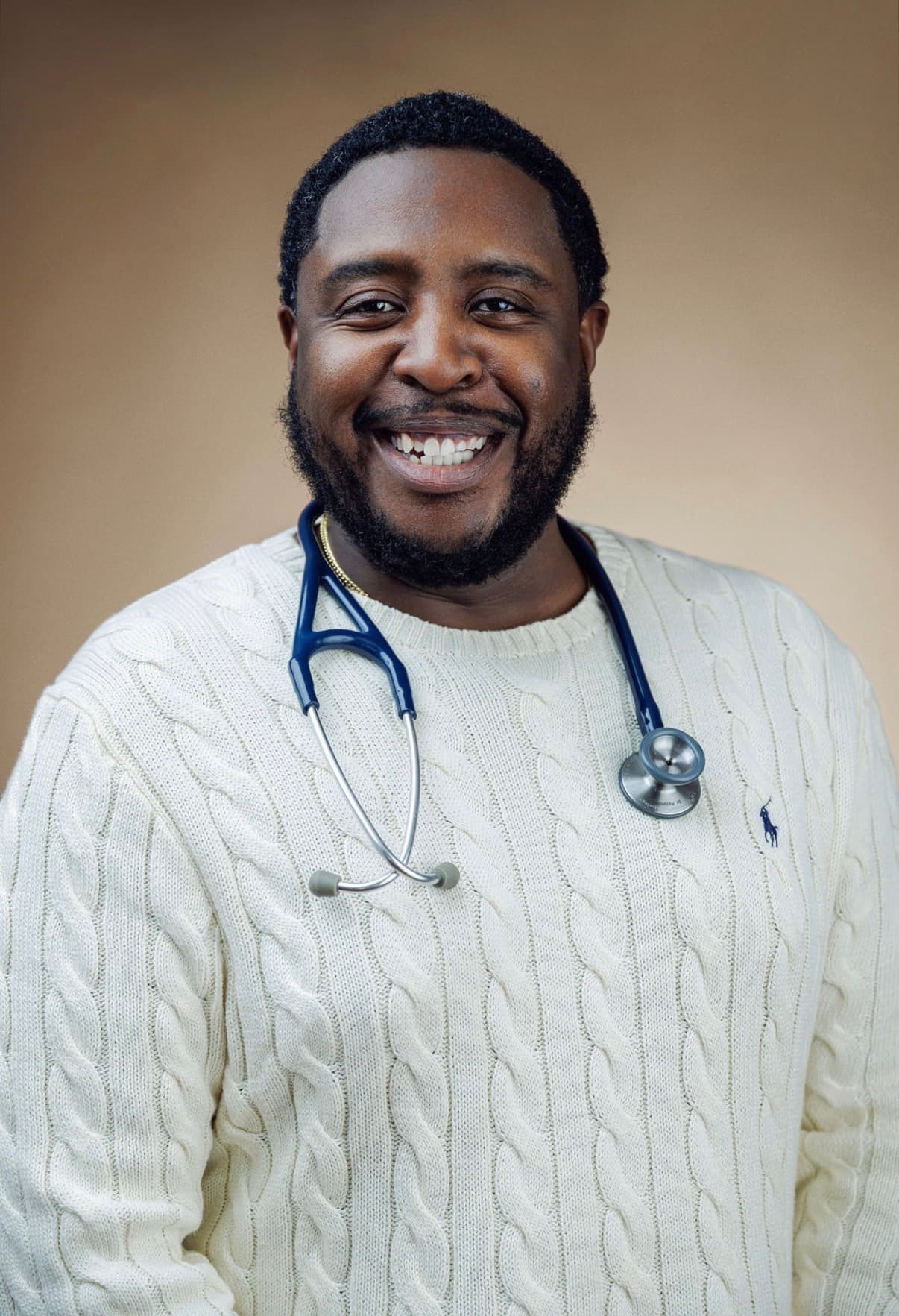 Christopher Hyppolite in a cream sweater with a stethoscope